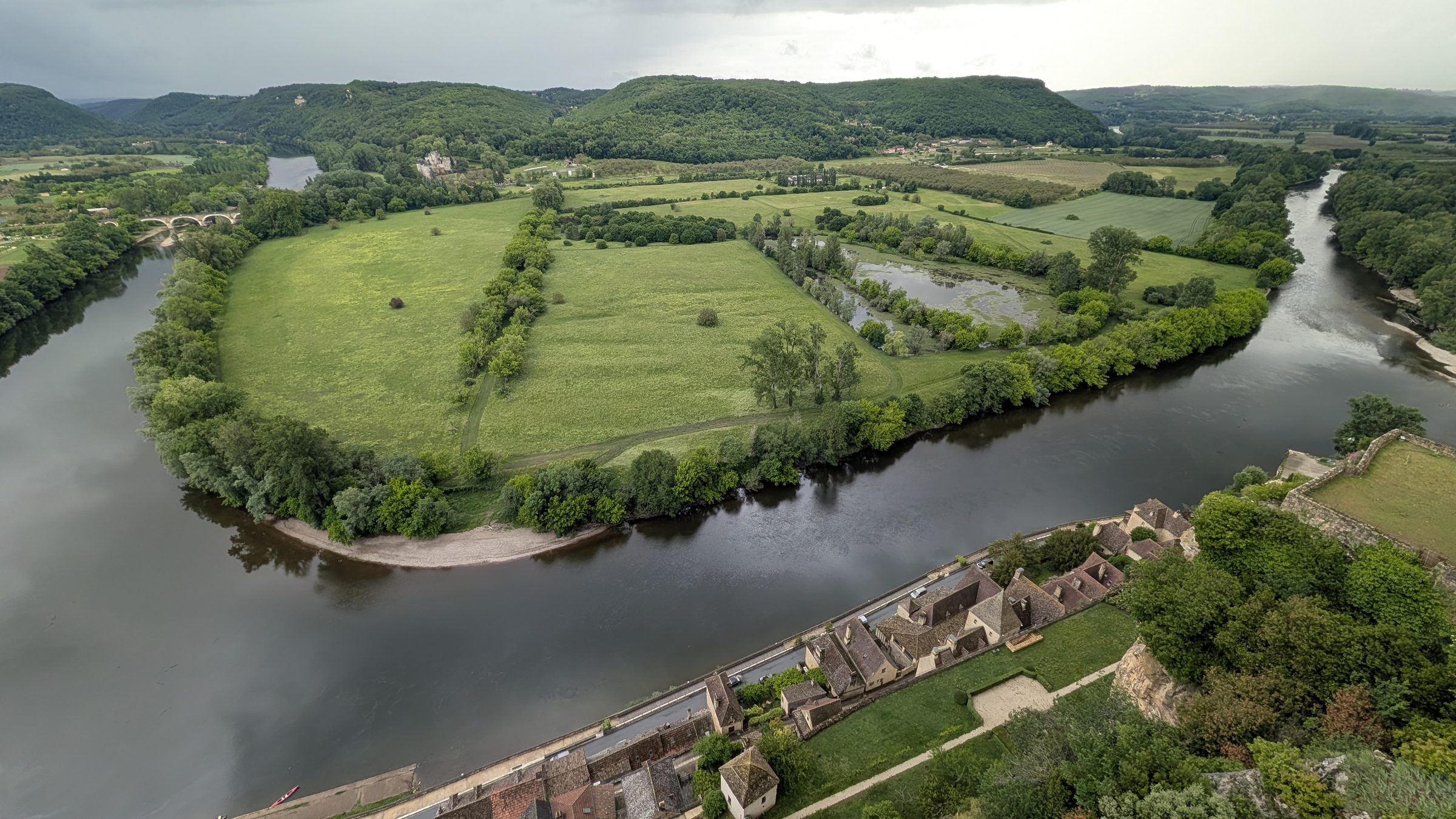 The Dordogne looping round green meadows below Beynac, seen from the château above the village rooftops