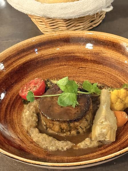 A round of meat in a glossy sauce with artichoke, tomato and aubergine purée, in a brown glazed bowl