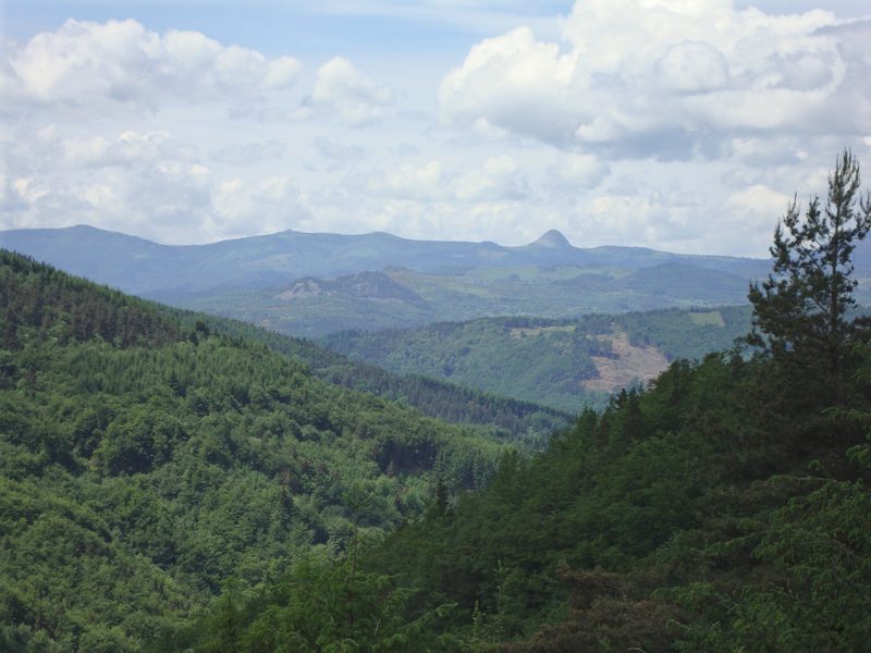 Forested hills and valleys around Saint-Agrève, with distant peaks under summer clouds